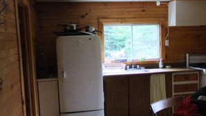 Eine kleine Küche mit Holzwänden, einem weißen Kühlschrank, einer Spüle und einem Fenster.