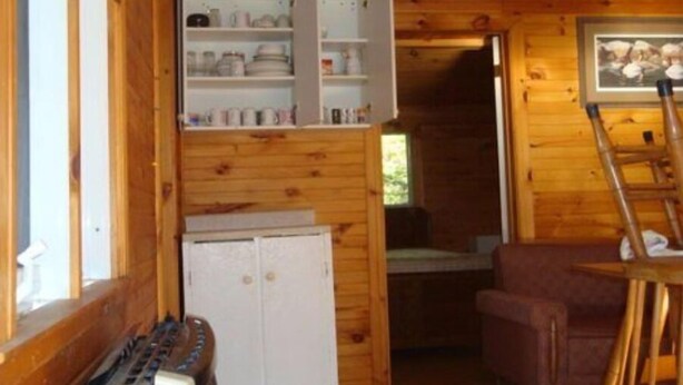 Ein Holzblockhaus-Innenraum mit Schlafkoje, einer kleinen Küchenzeile und einem Essbereich.