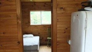 Ein Zimmer in einer Holzhütte mit einem Bett, einem Stuhl und einem Kühlschrank.