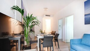 Una sala de estar moderna con un sofá azul, una mesa de comedor con sillas y una planta grande en maceta.