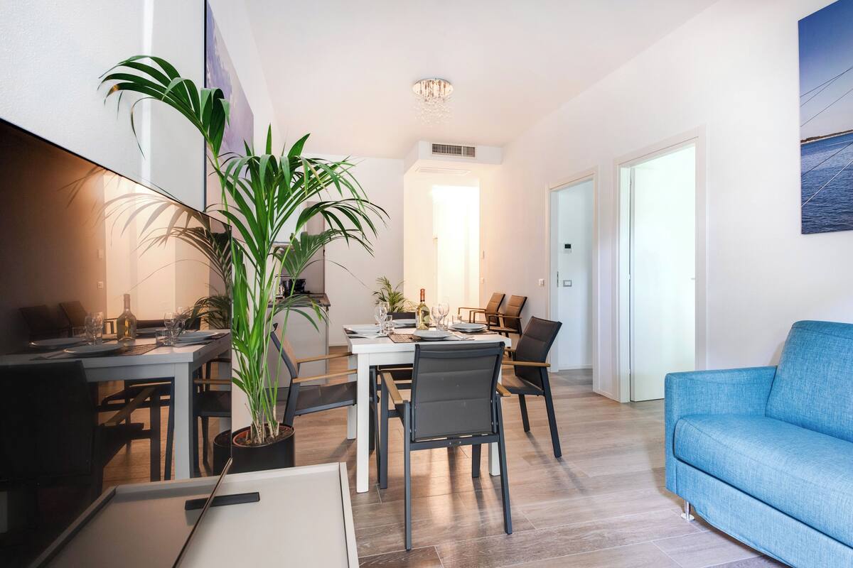 A modern living room with a blue sofa, a dining table set with chairs, and a large potted plant.