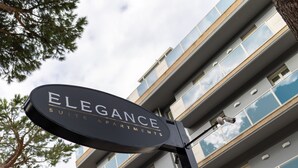 Señalización de 'Elegance Suite Apartments' con un edificio moderno de fondo.