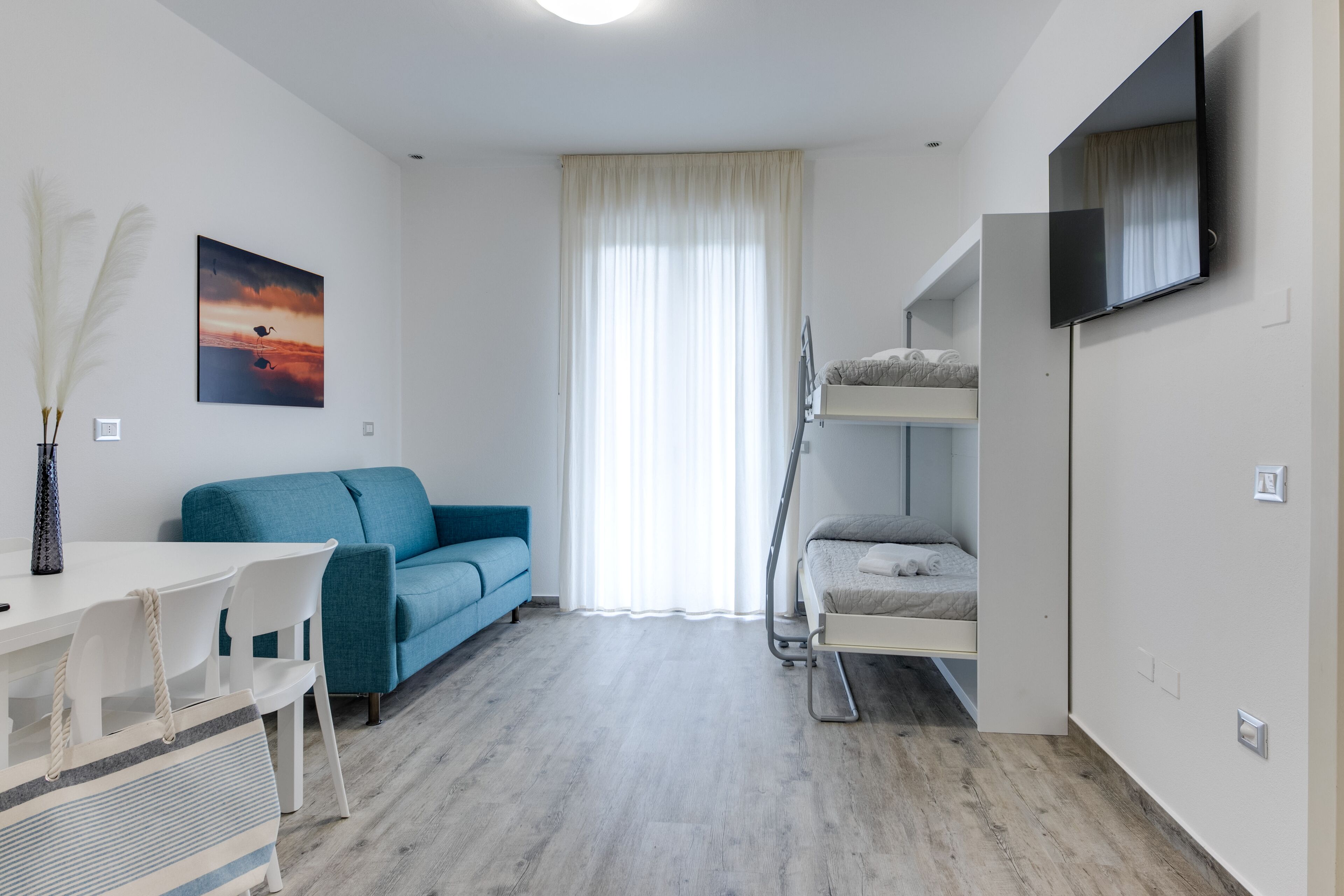 A modern room with a bunk bed, a sofa, a dining table, and a TV mounted on the wall.