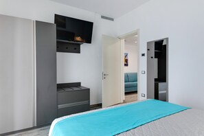 Un dormitorio moderno con una cama, un armario, un televisor y una puerta que da a otra habitación.