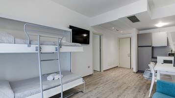 Ein modernes, gut beleuchtetes Zimmer mit Etagenbetten, einem Flachbildfernseher, einer Küchenzeile und einem blauen Stuhl.