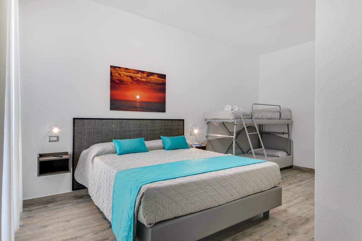 A bedroom with a bed, a bunk bed, a painting, and a nightstand.
