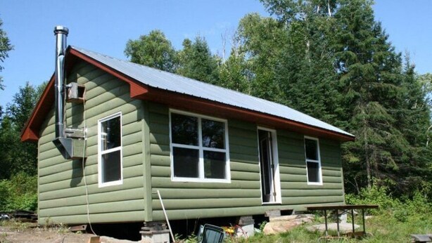 A green wooden house with a red roof, a chimney, and a front porch. - Hunting camp #10 (Egan-Sud)