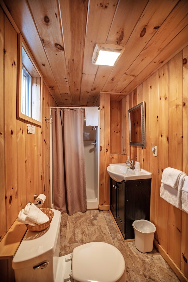 A wooden-paneled bathroom with a toilet, sink, and shower. - Pemi Cabins (Lincoln)