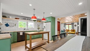 A modern kitchen with green cabinets, a wooden dining table, and red pendant lights. - Pemi Cabins (Lincoln)