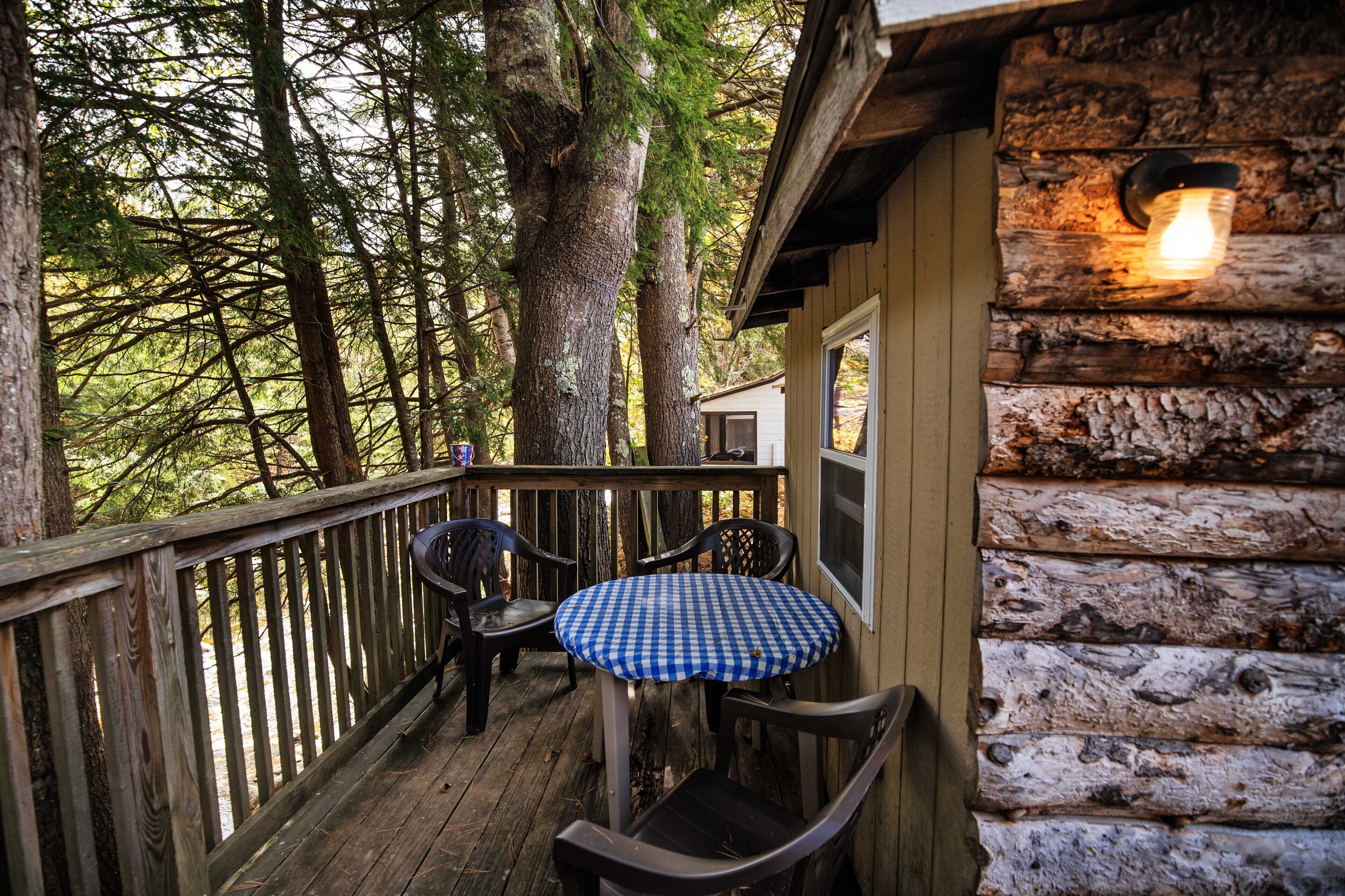 A wooden deck with a checkered table and chairs, surrounded by trees.