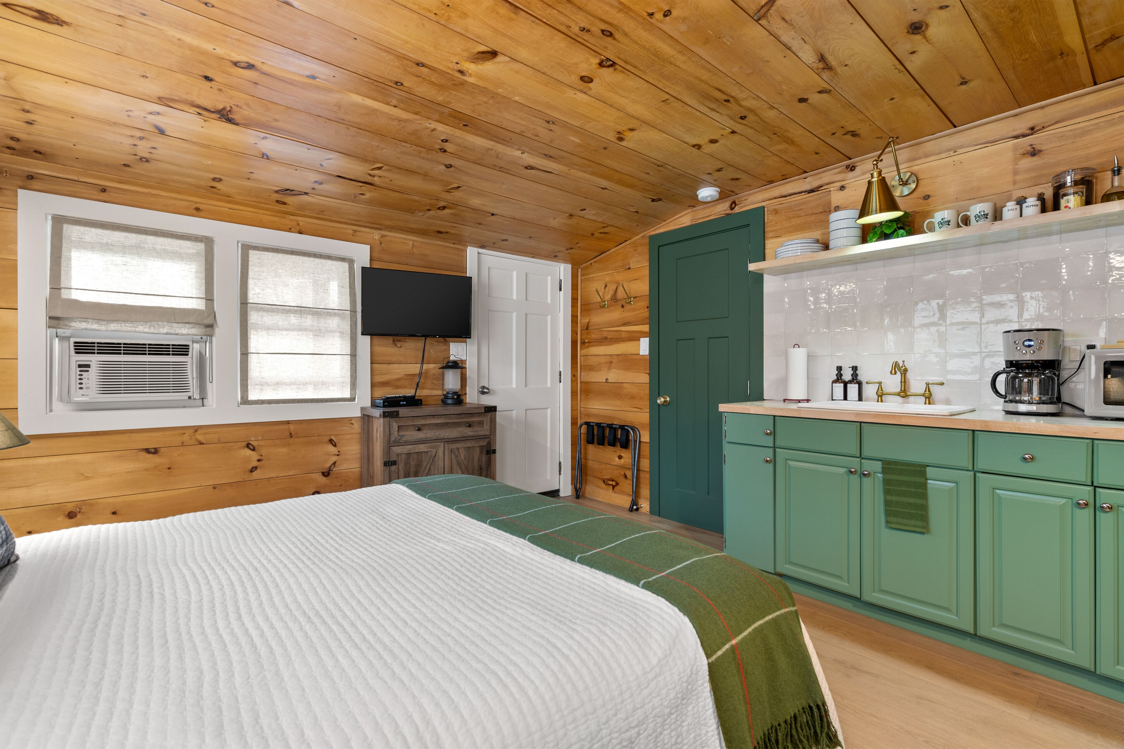 A cozy cabin-style room with a bed, a kitchenette, and a green door.