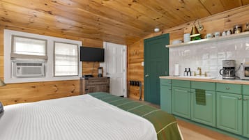 A cozy cabin-style room with a bed, a kitchenette, and a green door.