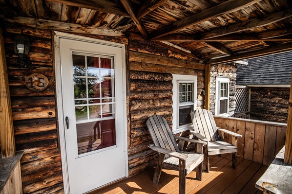 A log cabin with a wooden deck, two Adirondack chairs, and a door with a window.