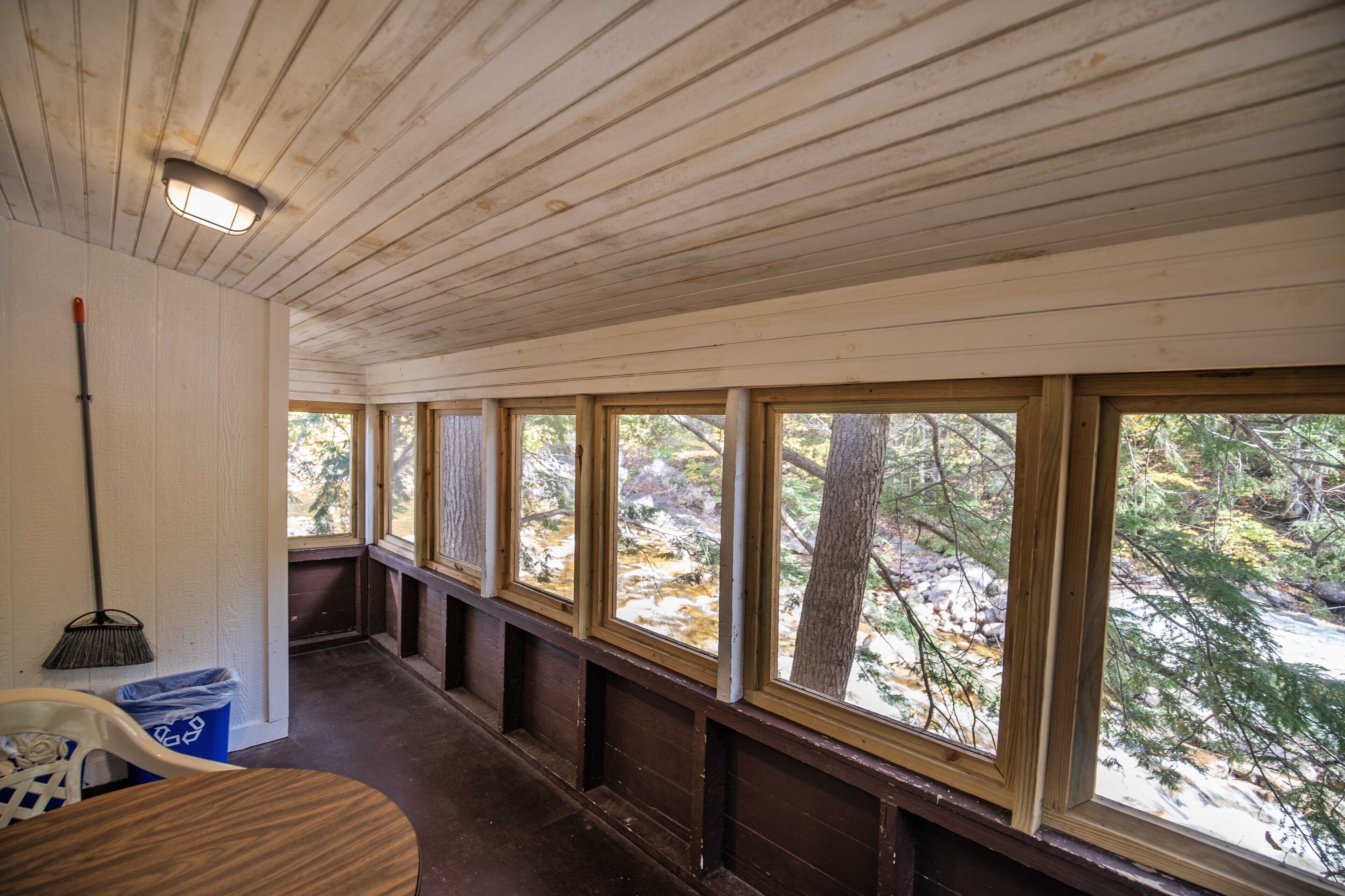 A corridor with wooden walls and windows overlooking a forested area.