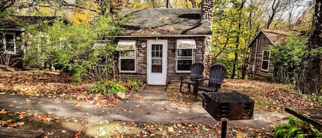 A rustic cabin with a wooden door, a bench outside, and a gravel path leading to it.