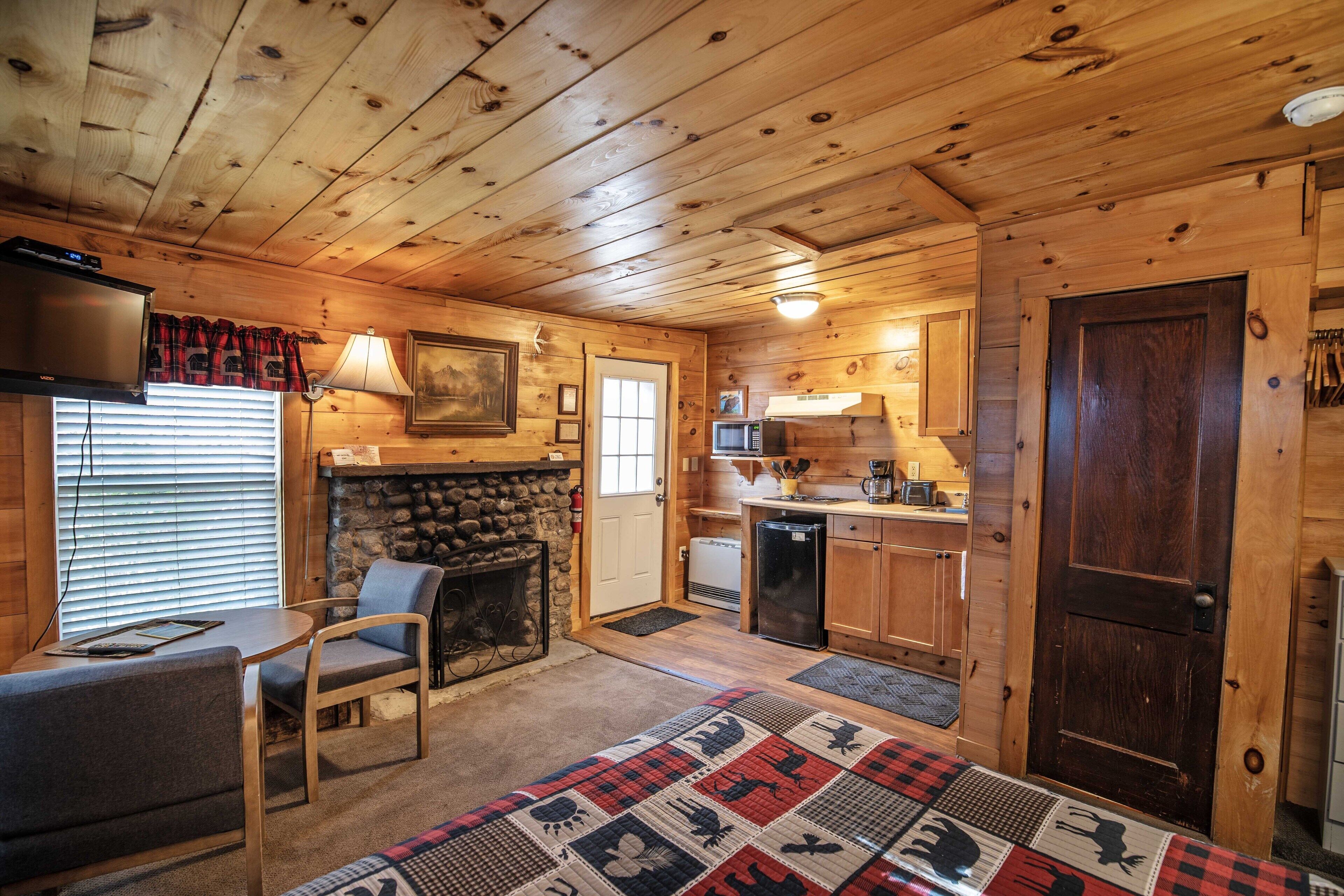 Ein gemütliches Blockhaus-Interieur mit Kamin, Fernseher, Küchenzeile und Essbereich.