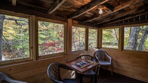 A wooden cabin with large windows, a table, and two chairs. - Pemi Cabins (Lincoln)