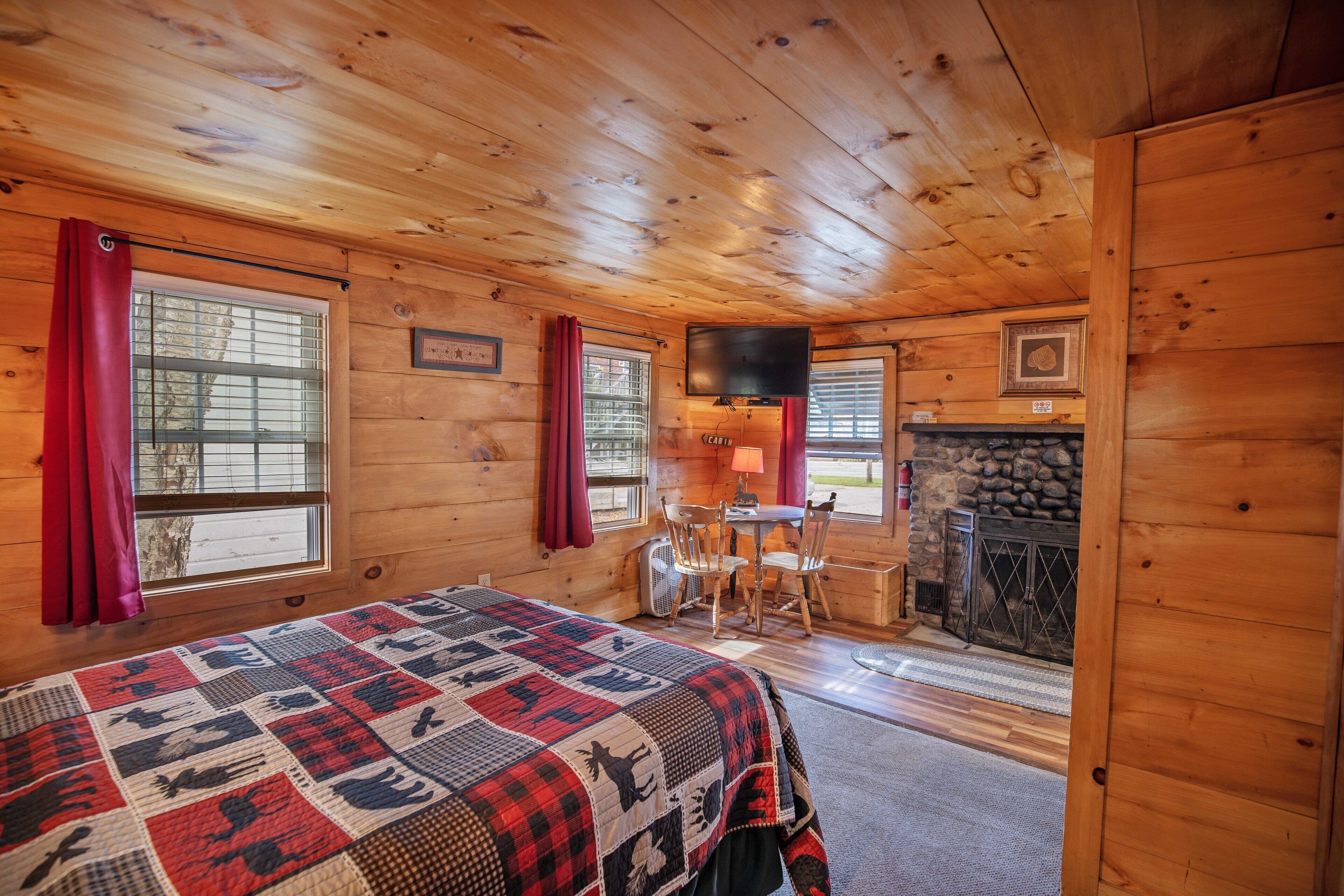 A cozy cabin room with a bed, a fireplace, a television, and a dining area.