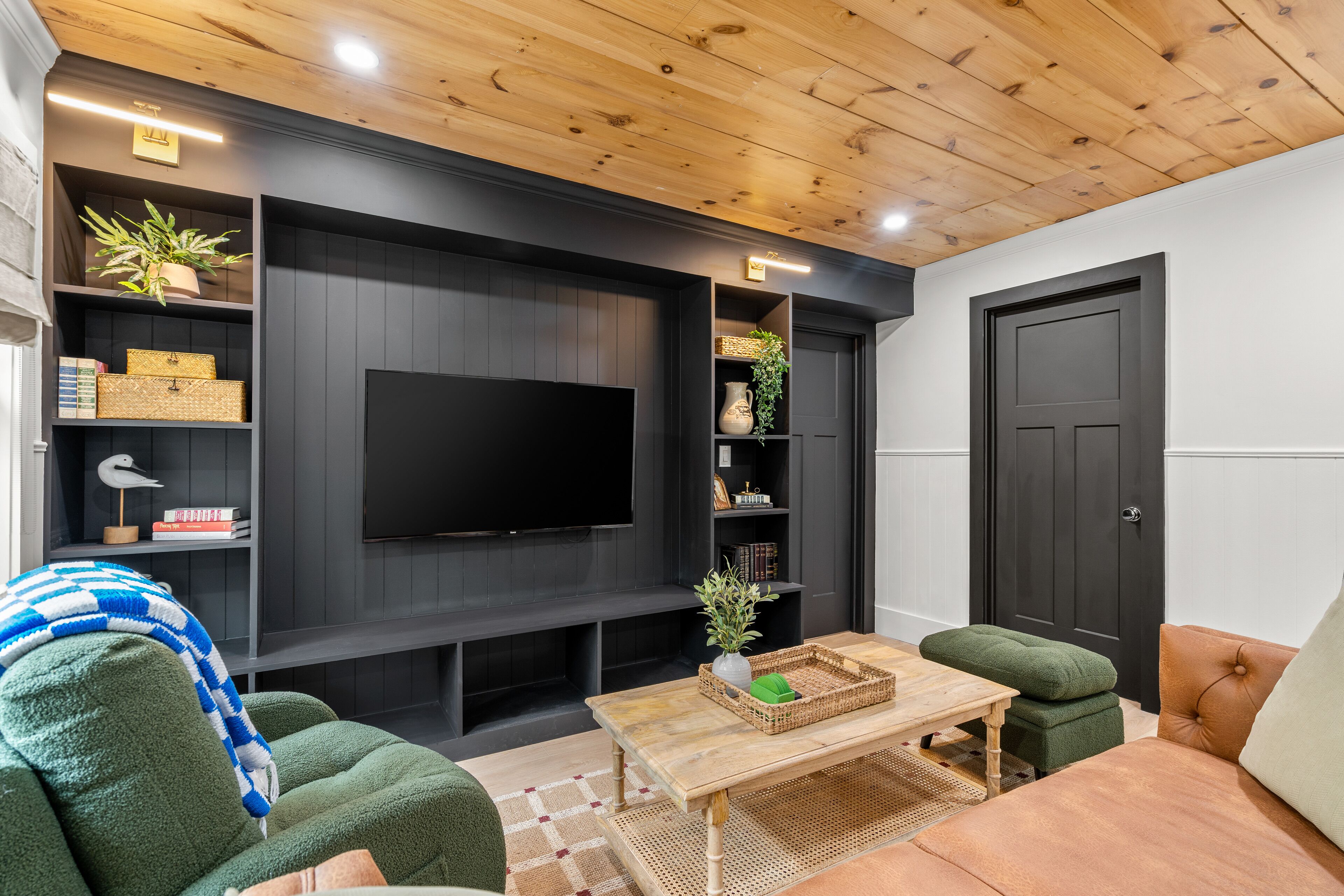 Una sala de estar moderna con televisor de pantalla plana, paneles de madera oscura, sofás verde y naranja, y una mesa de centro de madera.