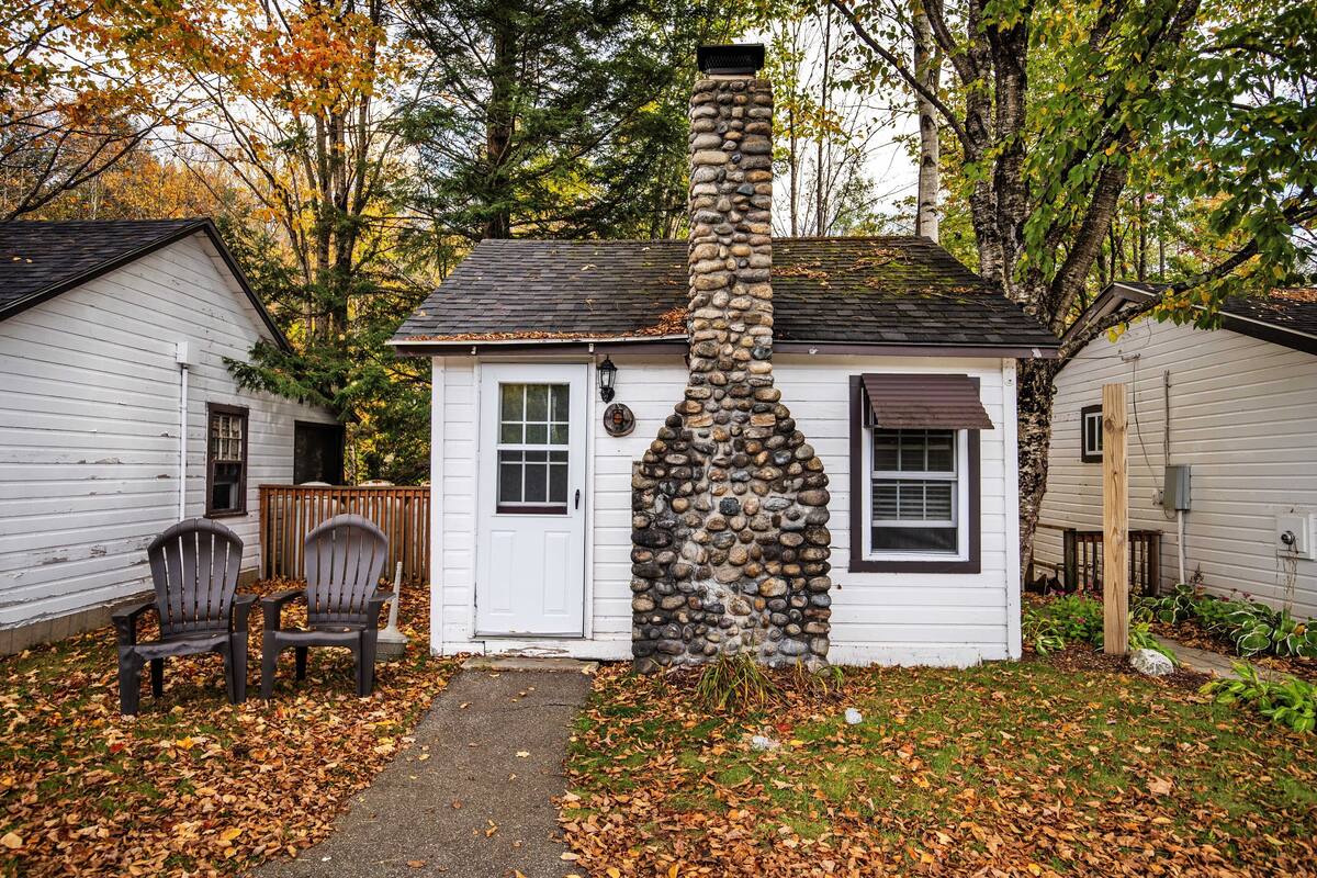 Una pequeña casa de piedra con fachada blanca, dos sillas Adirondack afuera y un sendero que lleva a la puerta.