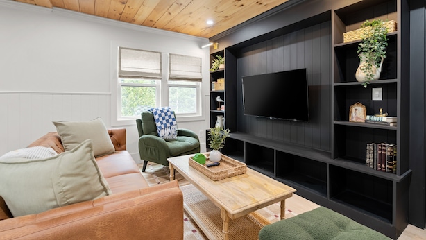 A living room with a wooden ceiling, a black entertainment unit, a green armchair, a brown leather sofa, and a flat-screen TV. - Pemi Cabins (Lincoln)