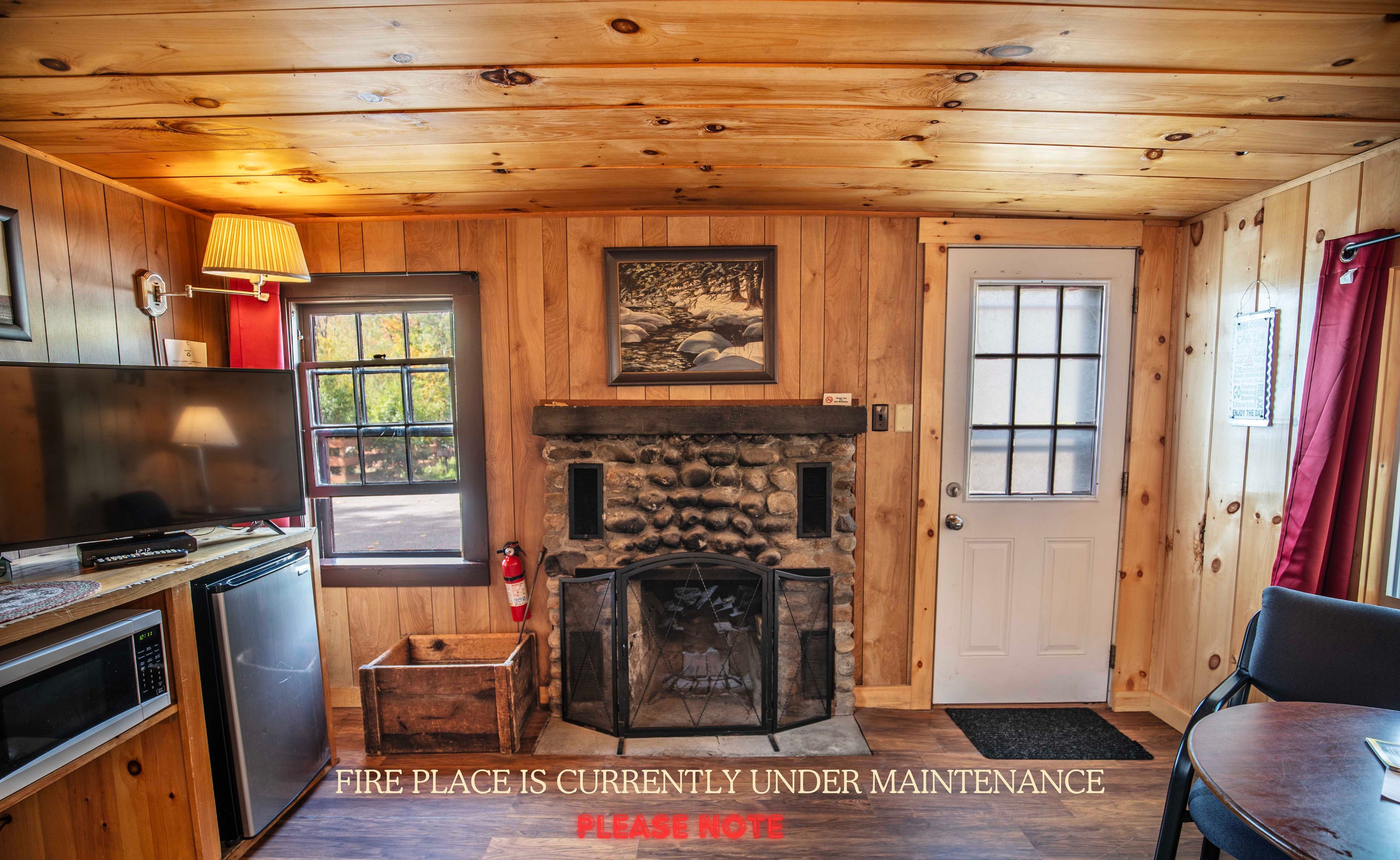 A cabin interior with a stone fireplace, wooden walls, a television, and a fireplace under maintenance sign.