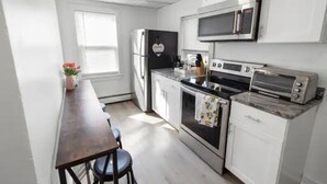Een moderne keuken met witte kasten, een roestvrijstalen koelkast, een magnetron, een oven en een broodrooster.