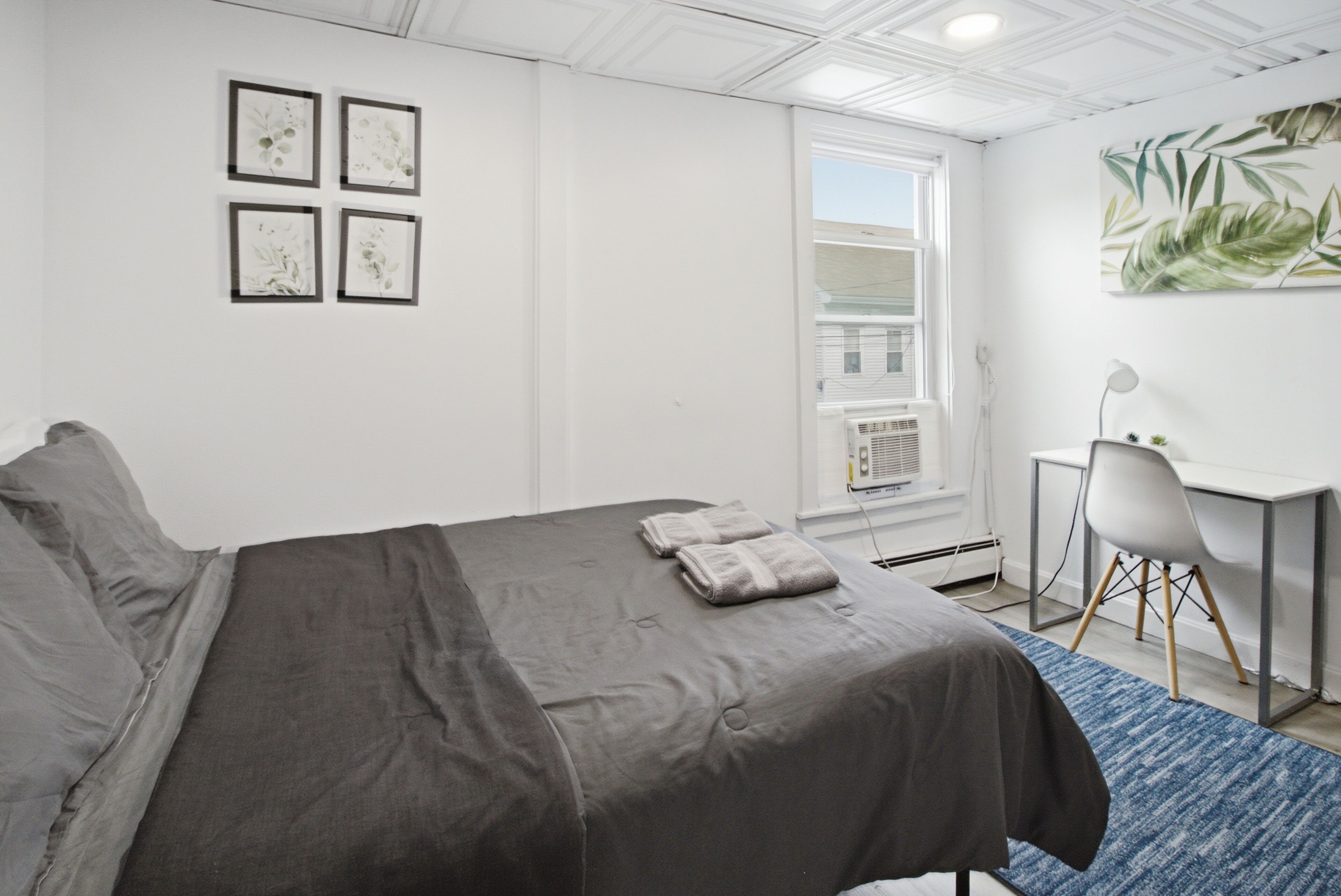 A bedroom with a bed, a desk, a chair, a window, and wall art.