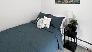 Een slaapkamer met een bed, kussens, een nachtkastje met een lamp, en een schilderij aan de muur.