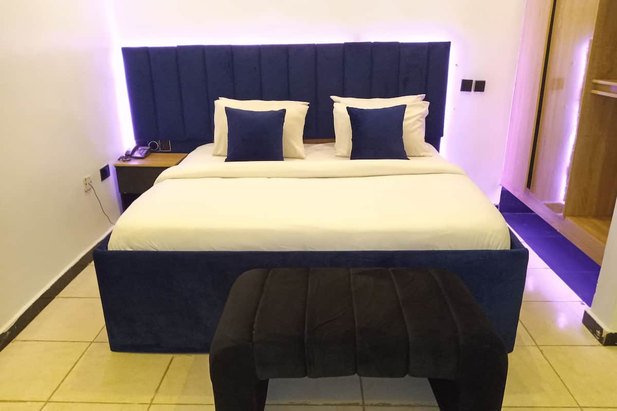 Quarto de hotel com uma cama grande, uma mesa de cabeceira e um banco em frente à cama.