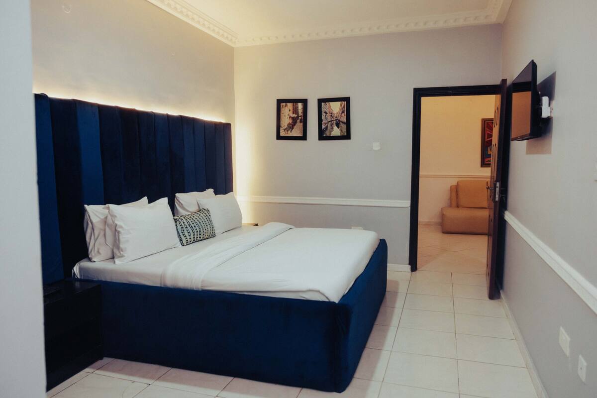 Um quarto com cama, mesa de cabeceira e porta que dá para outro cômodo.
