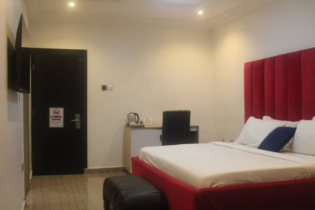 Quarto de hotel com cama, escrivaninha, cadeira e televisão presa na parede.