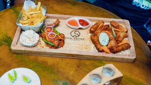Ein Holztablett mit verschiedenen gebratenen Speisen, darunter Frühlingsrollen und Pommes, dazu Dipsaucen und Krautsalat.