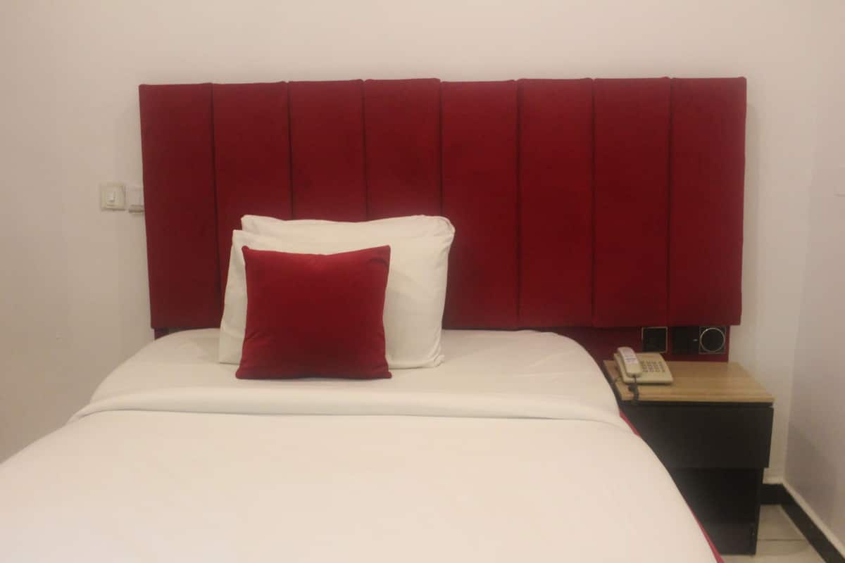 Quarto de hotel com cabeceira vermelha, roupa de cama branca, travesseiro vermelho e mesa de cabeceira com telefone.