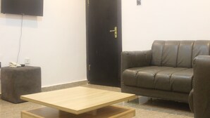 Ein Zimmer mit einer Couch, einem Couchtisch, einem an der Wand montierten Fernseher und einer Tür mit goldenem Griff.