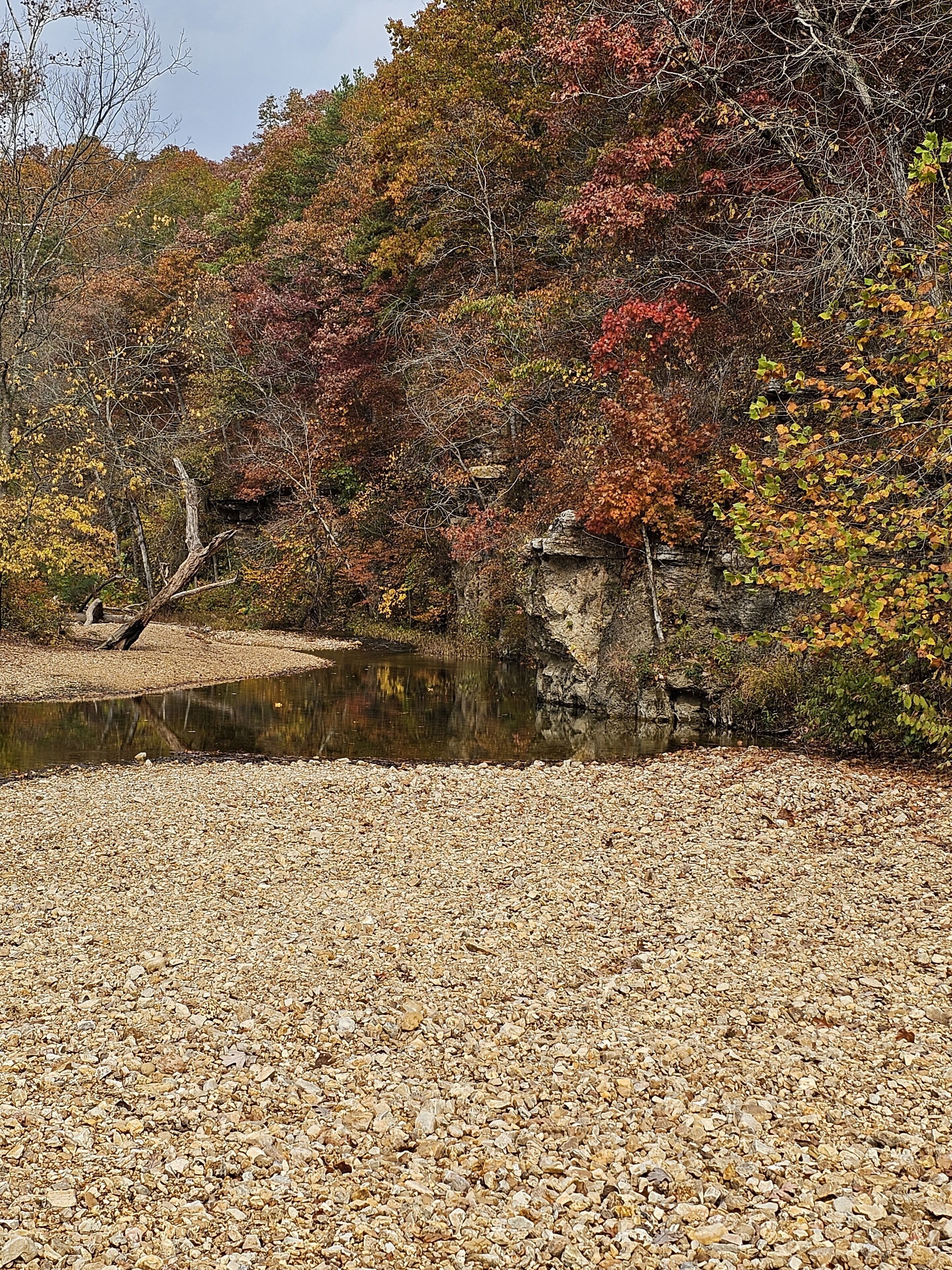 Paisaje natural con un primer plano de guijarros, una masa de agua pequeña y un afloramiento rocoso.