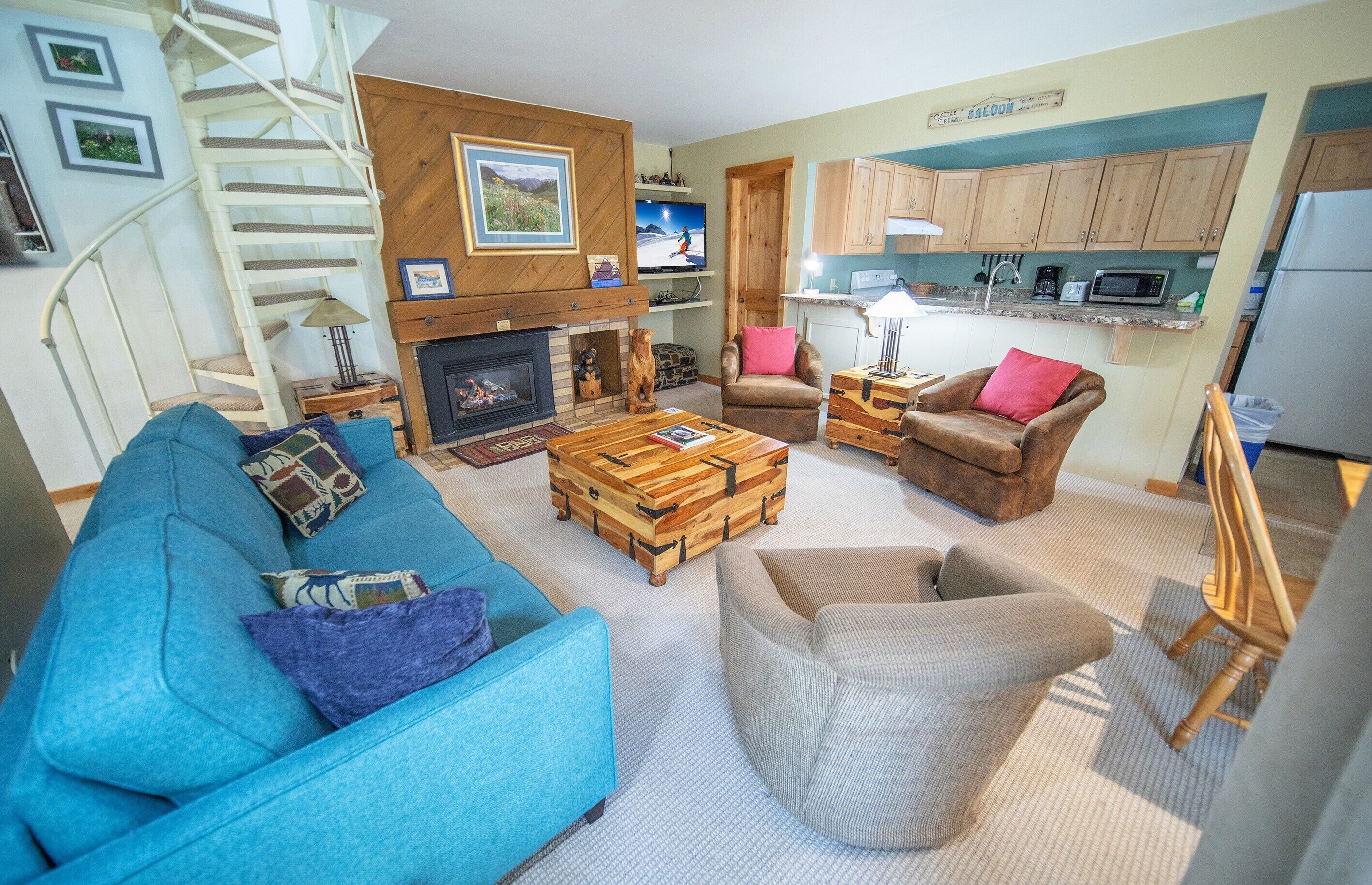 Ein Wohnzimmer mit einem blauen Sofa, einem Holztisch, einem Kamin, einem Fernseher und einer Küchenzeile mit Holzschränken und einer Mikrowelle.