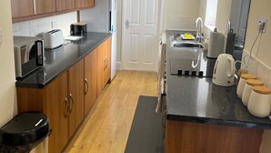 A compact kitchen with wooden cabinets, a black countertop, a stainless steel trash bin, and a black mat on the floor. - Norton Serviced Apartments (Stockton-on-Tees)