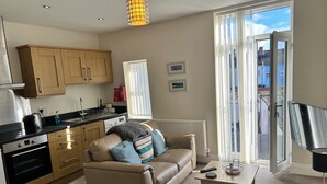 A modern apartment with a kitchen, a living area with a sofa and armchairs, a dining table, and a balcony with a view. - Norton Serviced Apartments (Stockton-on-Tees)