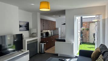 A modern living room with a flat-screen TV, a sofa, a coffee table, and a dining area with a kitchen in the background.