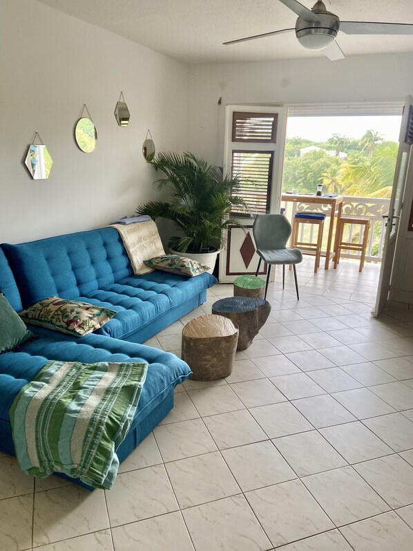 Relax in a spacious living area with a plush sofa, potted plant, and ceiling fan for comfort.