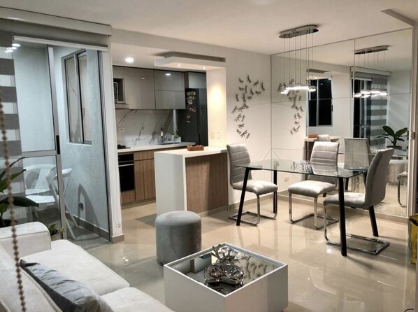 Contemporary living space with a central dining area and seating area, featuring a glass table, modern chairs, sofa, and coffee table.