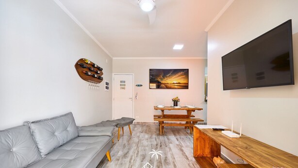 A modern living room with a grey sofa, wooden dining table, and a flat-screen TV mounted on the wall. - Madagascar (Ubatuba)