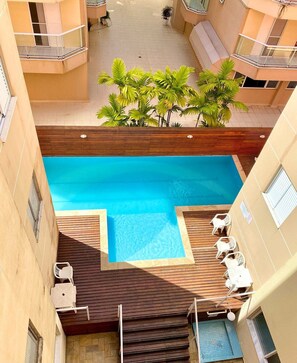 Una piscina en la azotea con solárium de madera, rodeada de edificios color beige y plantas en macetas.