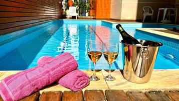 A poolside area with a wooden deck, a pink towel, two glasses of wine, and a champagne bottle in a metal bucket.