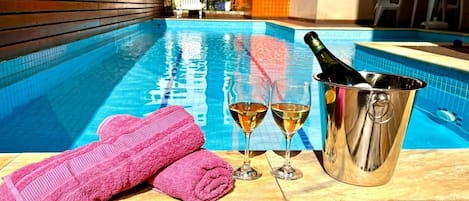 A poolside area with a wooden deck, a pink towel, two glasses of wine, and a champagne bottle in a metal bucket.