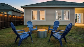 Ein Haus mit Garten, das eine Feuerstelle und vier blaue Adirondack-Stühle zeigt.