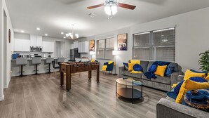 Ein modernes Wohnzimmer mit einem Tischfußballtisch, einem grauen Sofa mit blauen und gelben Kissen und einem Couchtisch.