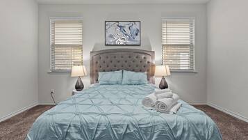 A bedroom with a large bed, two bedside lamps, a headboard, and a painting above the bed.