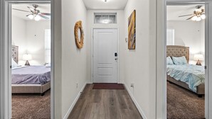 Ein Flur, der zu zwei Schlafzimmern führt, jeweils mit einem Bett, einem Deckenventilator und einem Fenster.